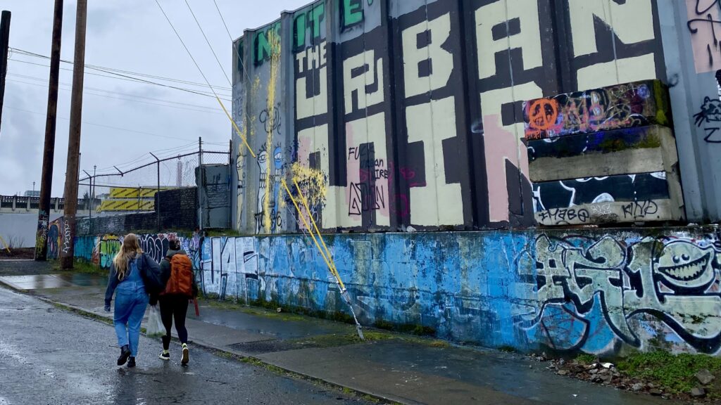 Two homeless outreach workers with Catholic Charities Portland walk past a graffitied wall in the city.