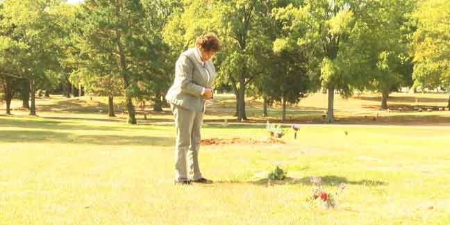 A woman stands by a grave, her head bowed in prayer.