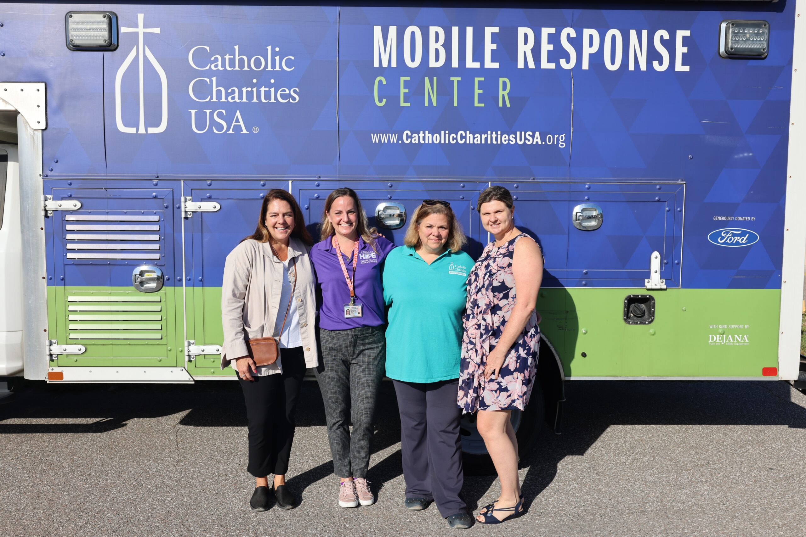 Kerry Alys Robinson (Catholic Charities USA president and CEO), Shannon Leigh (Catholic Charities Diocese of St. Petersburg), Kim Burgo (CCUSA vice president, disaster operations), and Maggie Rogers (executive director of Catholic Charities Diocese of St. Petersburg) pose in front of the CCUSA mobile response center during a visit to Pinellas Hope after Hurricane Helene.