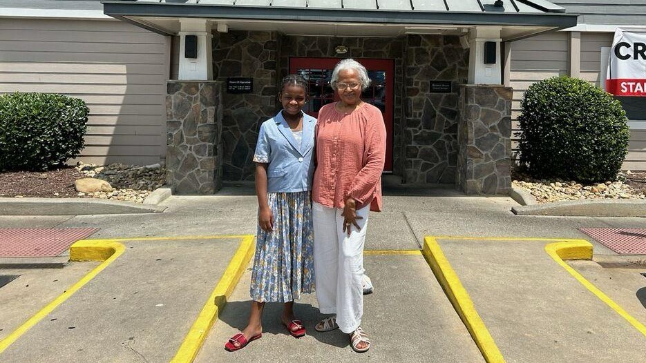 A mentor with the Refugee Youth Mentoring program at Catholic Charities Atlanta poses with her mentee in front of a restaurant. Both are smiling in the sunshine.